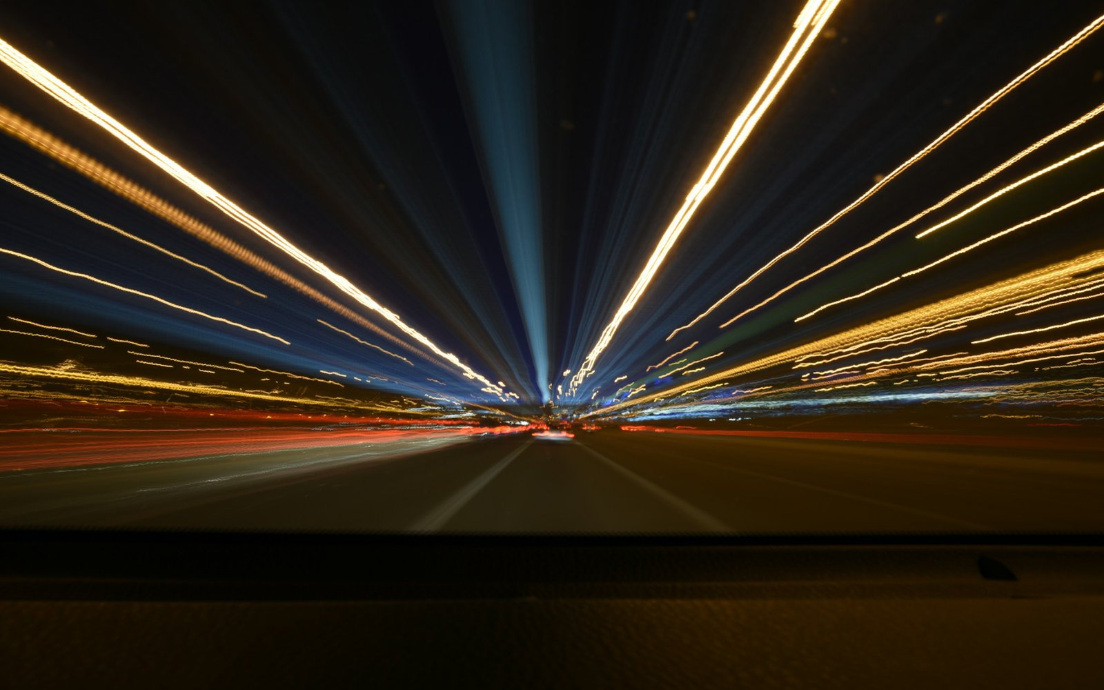Long-exposure night photo from a moving vehicle, with streaks of white, yellow, and red light radiating outward from a vanishing point down a dark highway. Photo by Tohidul Islam on Unsplash